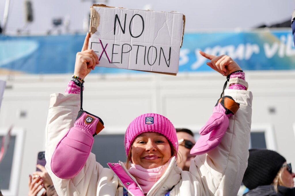 Annika Malacinski holding a protest sign in the snowy stands at the Winter Olympics
