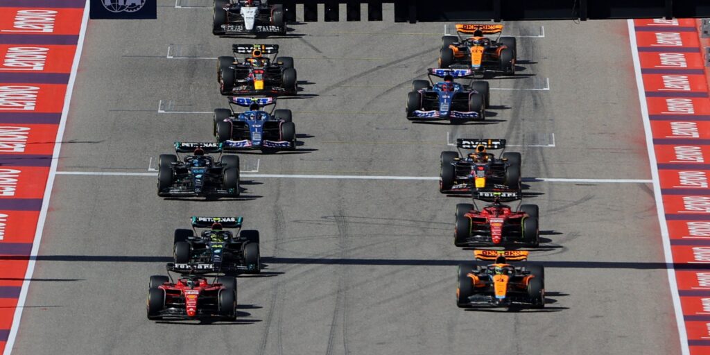 Adrian Newey looking concerned while speaking with Lance and Lawrence Stroll in the Aston Martin garage during F1 testing