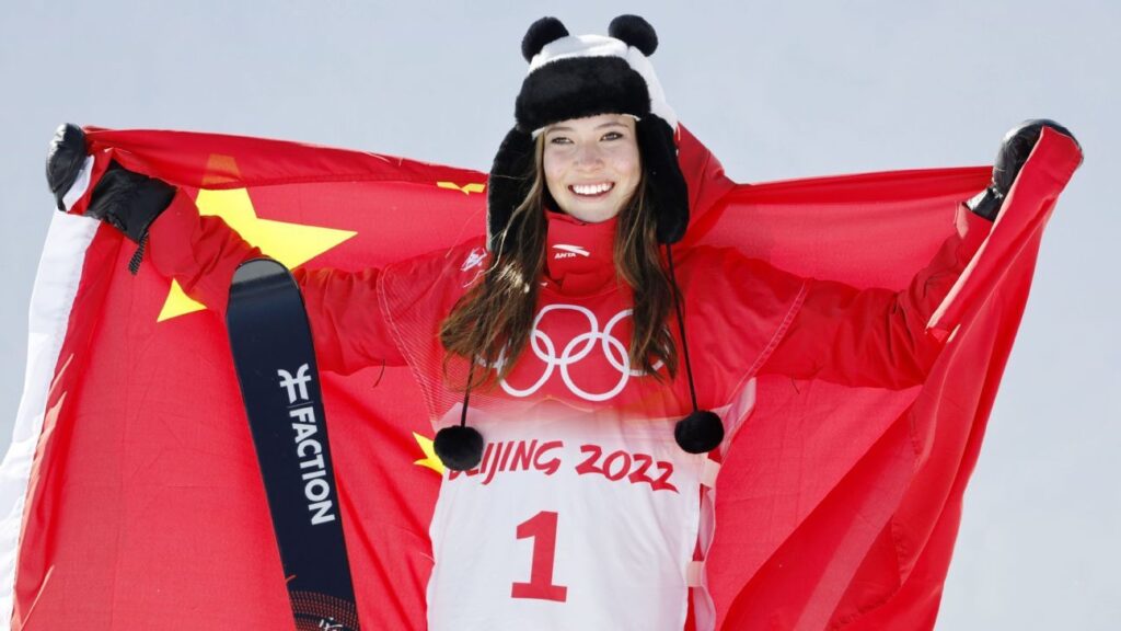 Eileen Gu holding her skis and smiling at the bottom of the slope after a freestyle skiing run