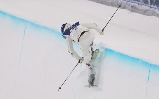 Eileen Gu holding her skis and looking towards the halfpipe course at the Winter Olympics