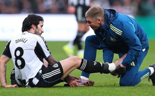 A football referee checking on an injured player receiving treatment on the pitch