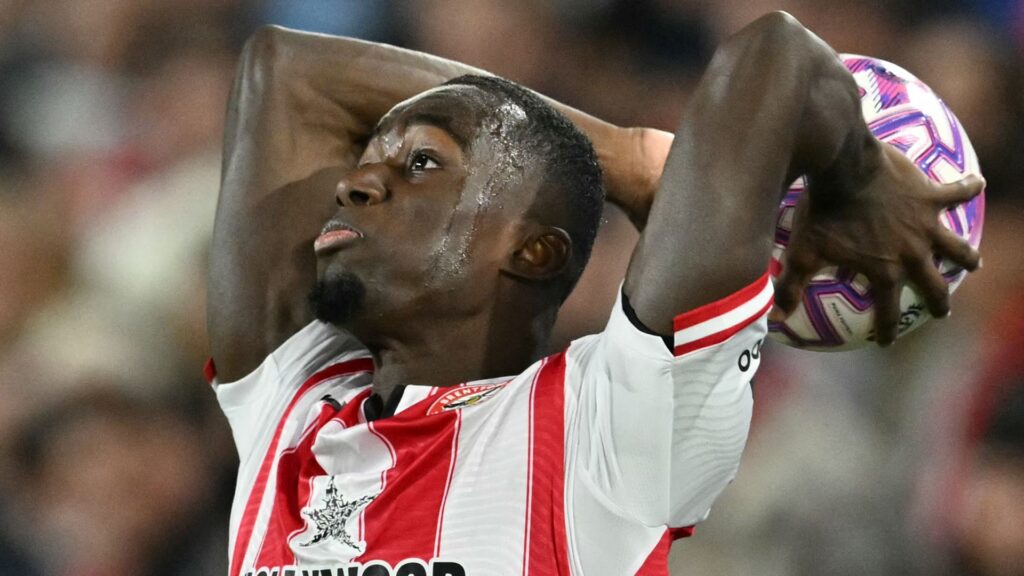 A football referee checking their watch while a player prepares to take a throw-in on the touchline