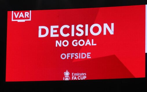 A football referee communicating with the VAR room via a headset while holding a yellow card during a match