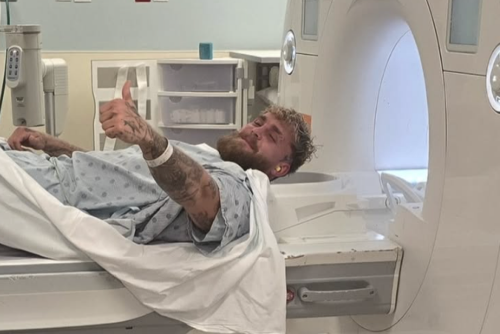 Jake Paul sitting in a hospital bed with a bandaged jaw alongside Jutta Leerdam