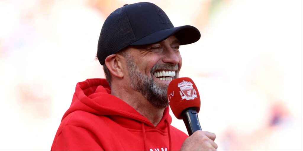 Jurgen Klopp smiling and waving to fans during a Liverpool trophy parade