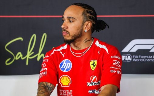 Lewis Hamilton wearing Ferrari team kit walking in the paddock with a serious expression