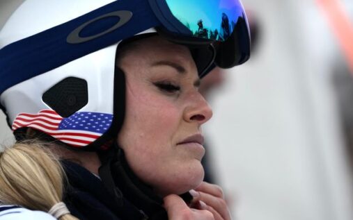 Lindsey Vonn inspecting a ski slope while wearing a helmet and goggles