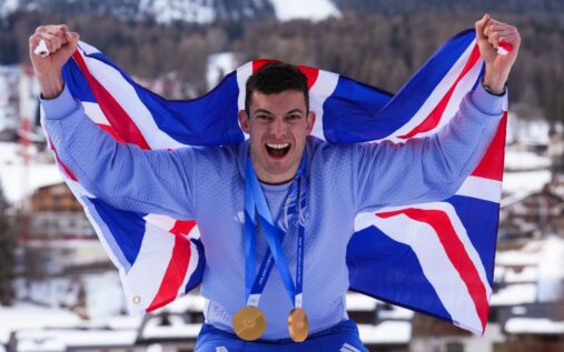 Matt Weston and Charlotte Bankes smiling in Team GB kit holding their gold medals