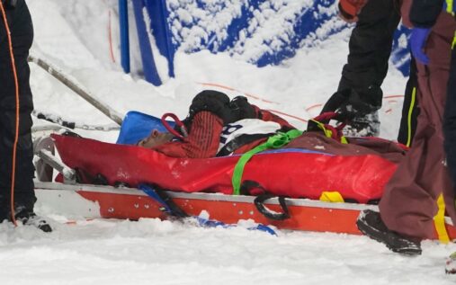 Close up of Mark McMorris wearing a snowboard helmet and goggles, looking determined against a snowy mountain backdrop