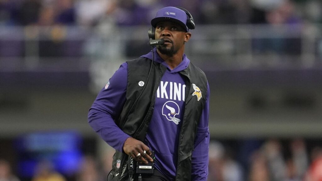 Brian Flores wearing a headset and team gear standing on the sidelines during an NFL game