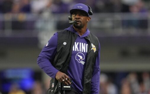 Brian Flores wearing a headset and team gear standing on the sidelines during an NFL game