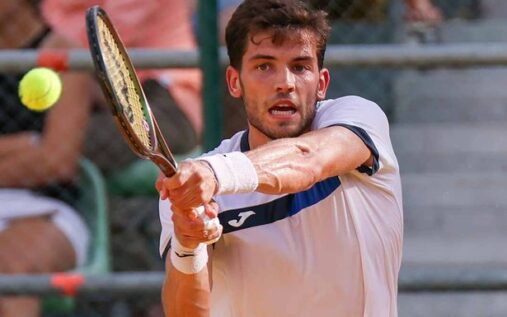 Nikolas Sanchez playing a forehand shot on a clay court during a tennis match