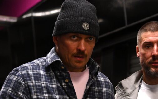 Oleksandr Usyk celebrating in the ring with heavyweight championship belts draped over his shoulders