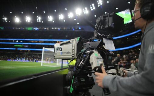 A television camera operator filming a live Premier League football match from the gantry