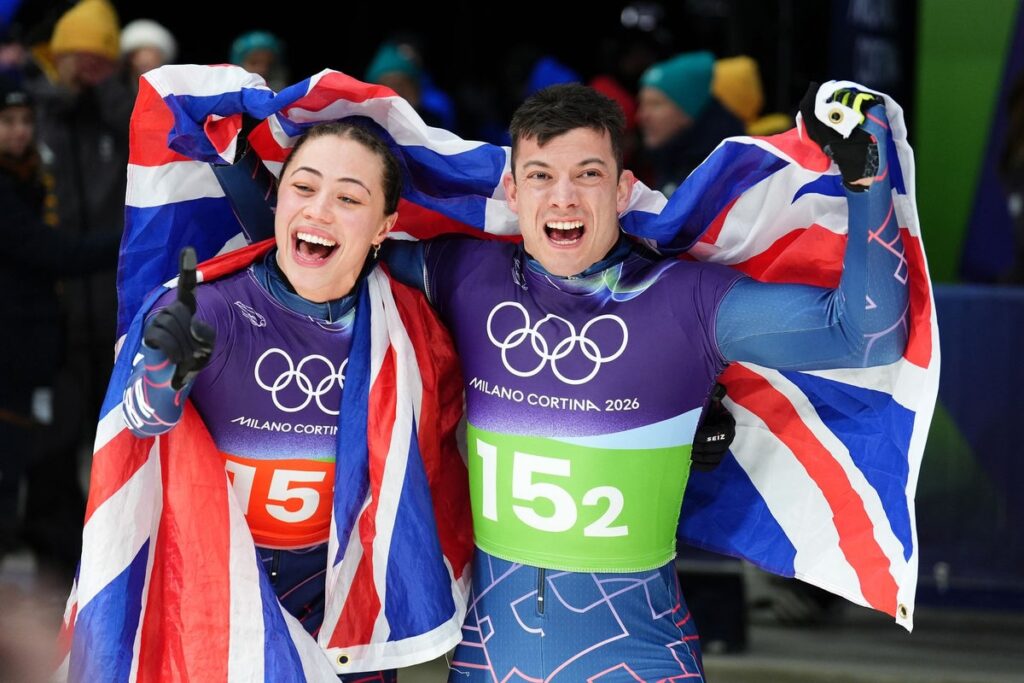 Matt Weston holding the Union Jack flag and smiling after winning a gold medal in the skeleton event