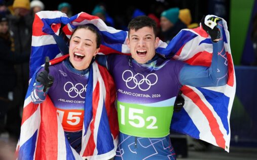 Matt Weston holding the Union Jack flag and smiling after winning a gold medal in the skeleton event