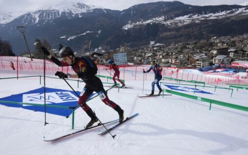 A ski mountaineering athlete ascending a steep snowy slope with skis attached to their backpack during a competition