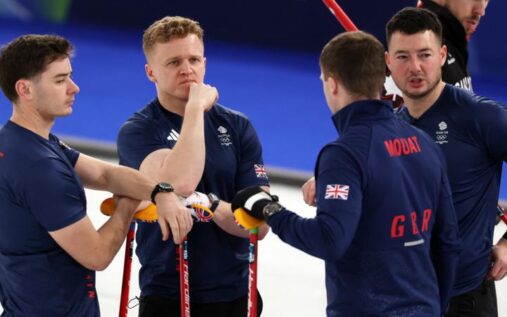 Bruce Mouat delivering a curling stone while teammates sweep the ice at the Cortina Curling Stadium
