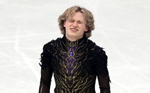 Mikhail Shaidorov celebrating his figure skating gold medal on the ice while Ilia Malinin looks on dejected.