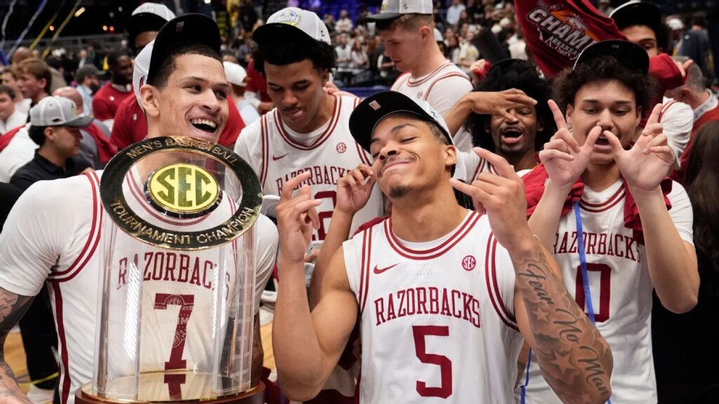 Darius Acuff Jr holds the SEC tournament trophy surrounded by celebrating Arkansas Razorbacks teammates