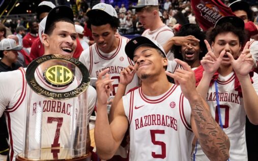 Darius Acuff Jr holds the SEC tournament trophy surrounded by celebrating Arkansas Razorbacks teammates