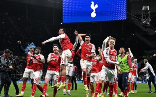 Arsenal fans celebrating in the stands with red and white scarves