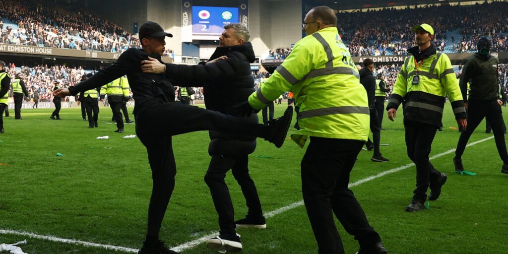 Police officers attempting to control a crowd on the pitch at Ibrox Stadium during the Rangers vs Celtic match