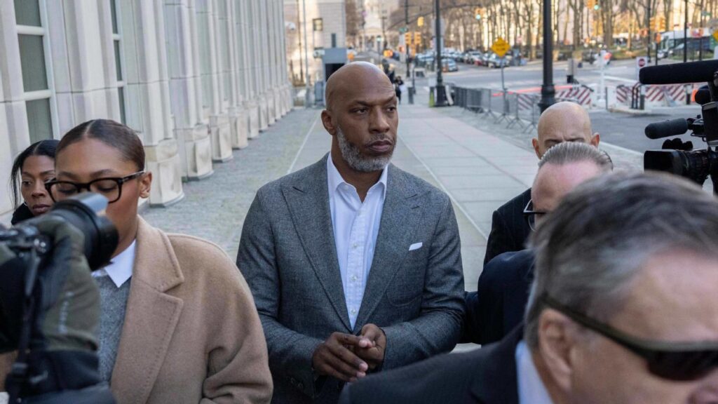 Chauncey Billups wearing a grey suit leaving a federal courthouse surrounded by cameras