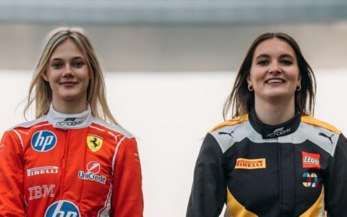 F1 Academy female drivers standing in their racing suits beside a track