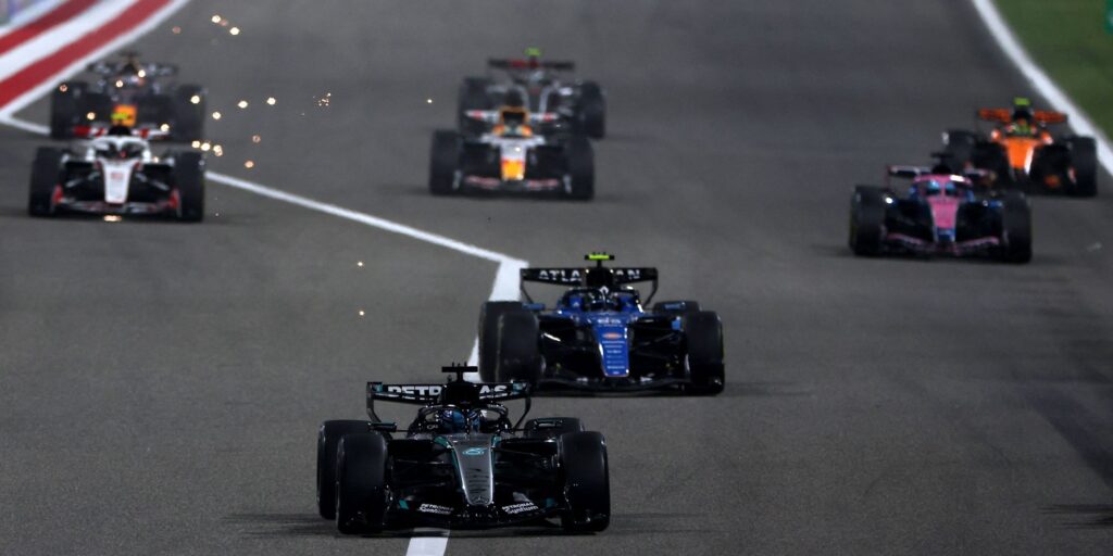 Formula 1 cars racing on a track under floodlights during a Middle Eastern Grand Prix