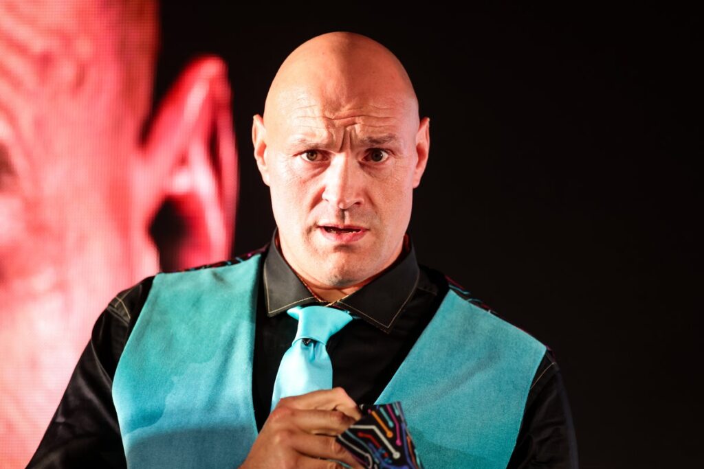 Fabio Wardley gesturing to the crowd during a weigh-in, wearing his WBO heavyweight championship belt