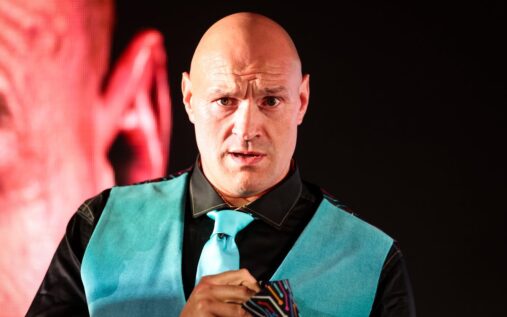 Fabio Wardley gesturing to the crowd during a weigh-in, wearing his WBO heavyweight championship belt