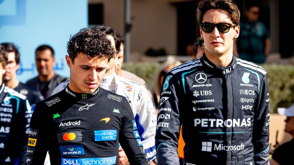 George Russell wearing Mercedes team cap and polo shirt speaking to media in the F1 paddock