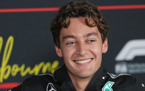 George Russell wearing Mercedes team kit speaking to the media in the paddock