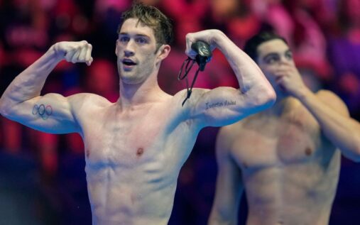 Hunter Armstrong celebrating a victory in the pool wearing a swimming cap and goggles