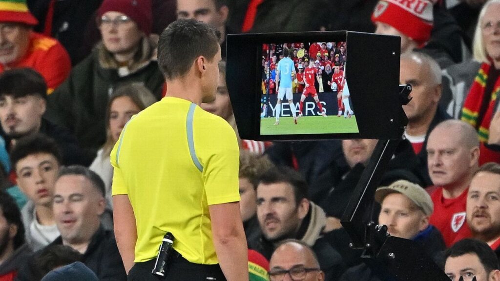 A referee looking at a watch while holding a football during a match