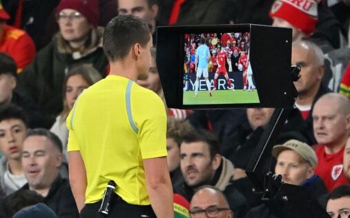 A referee looking at a watch while holding a football during a match