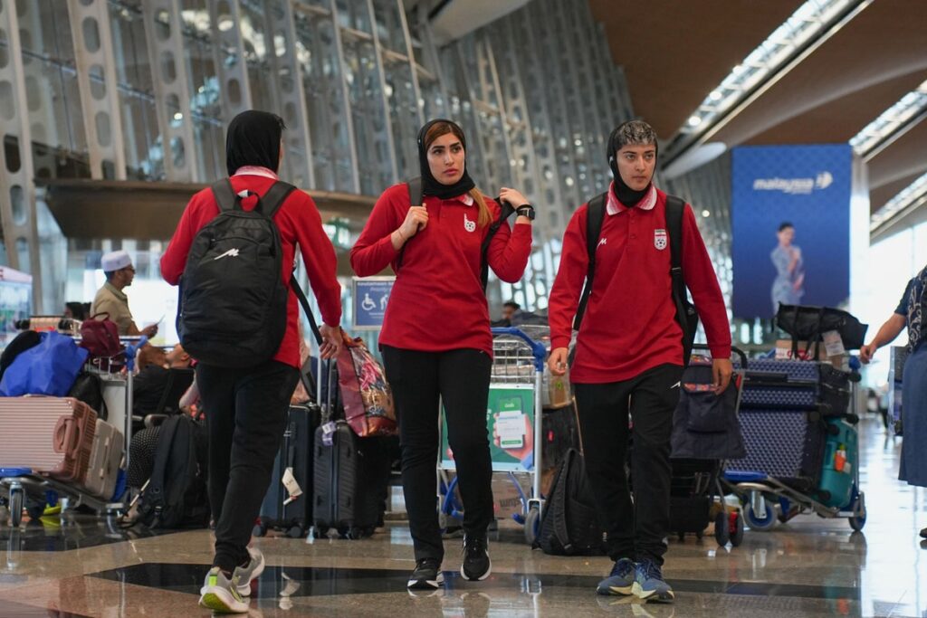 Members of the Iranian women's football team walking with their luggage
