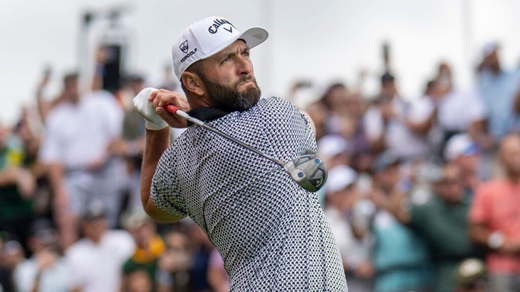 Jon Rahm wearing a golf cap and polo shirt looking disappointed on the golf course