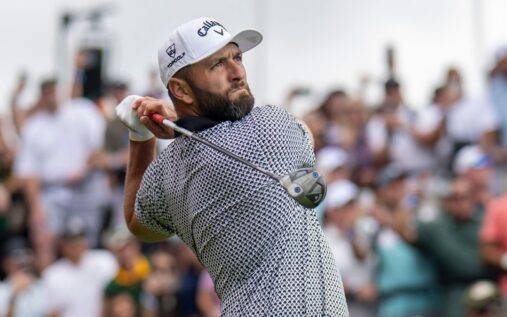 Jon Rahm wearing a golf cap and polo shirt looking disappointed on the golf course