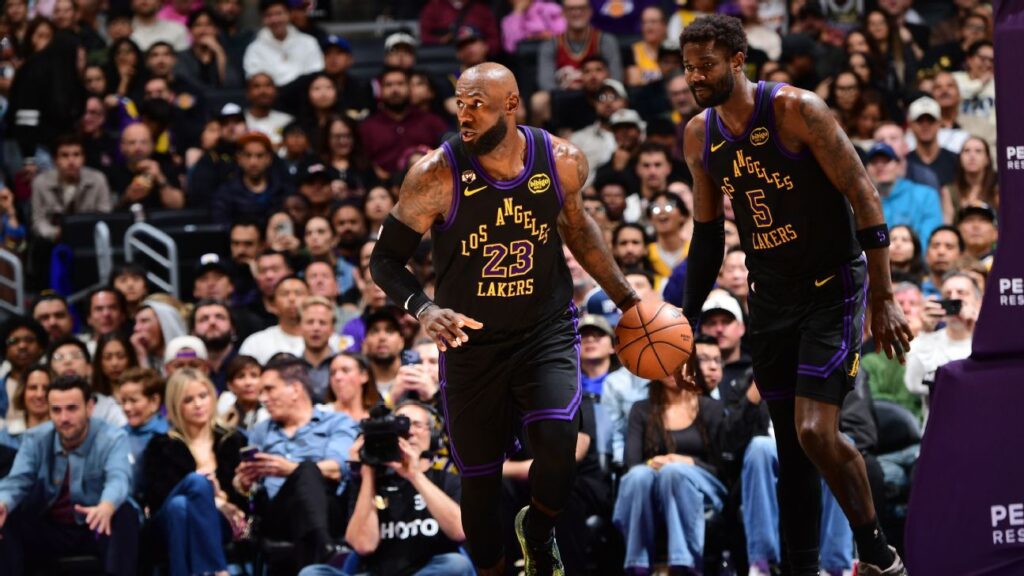 LeBron James wearing a Los Angeles Lakers jersey grimaces while holding his left elbow during an NBA game