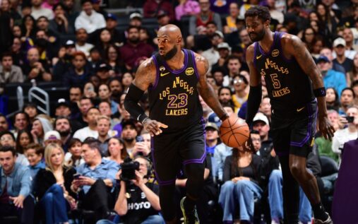 LeBron James wearing a Los Angeles Lakers jersey grimaces while holding his left elbow during an NBA game