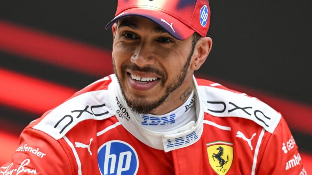 Lewis Hamilton in his red Ferrari race suit smiling confidently during a Formula 1 weekend