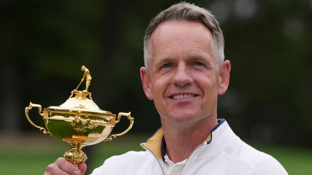 Luke Donald smiling and holding the Ryder Cup trophy while celebrating with Team Europe teammates