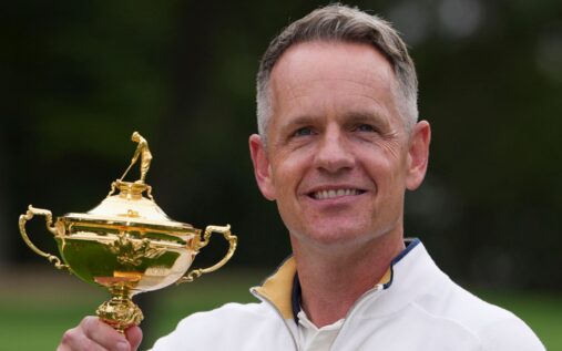 Luke Donald smiling and holding the Ryder Cup trophy while celebrating with Team Europe teammates