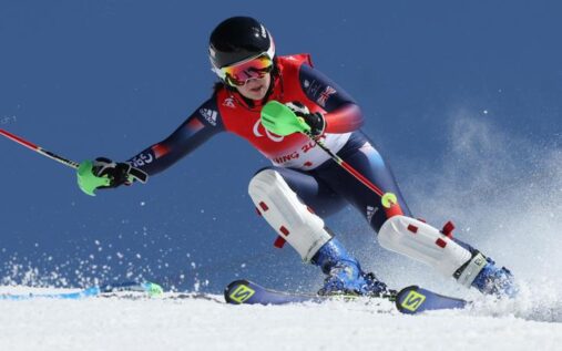 Menna Fitzpatrick wearing Team GB kit and ski helmet smiling on a snowy mountain slope alongside her guide.