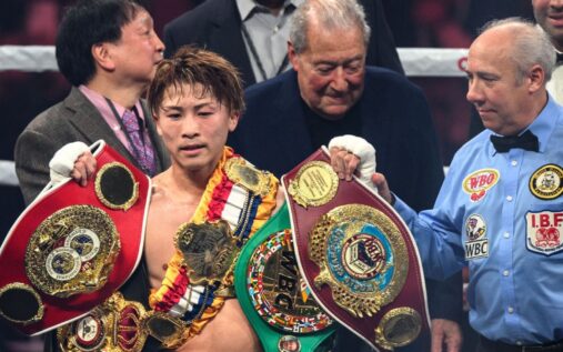 Naoya Inoue standing in the boxing ring holding his championship belts