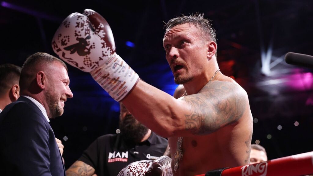 Oleksandr Usyk standing in the boxing ring holding his unified heavyweight championship belts