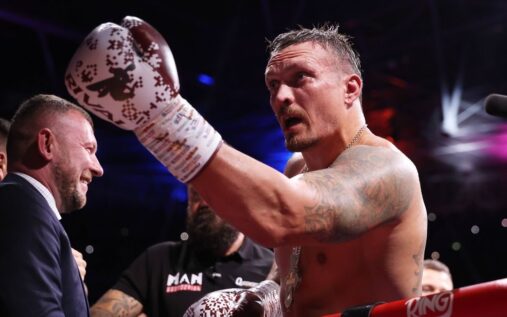Oleksandr Usyk standing in the boxing ring holding his unified heavyweight championship belts