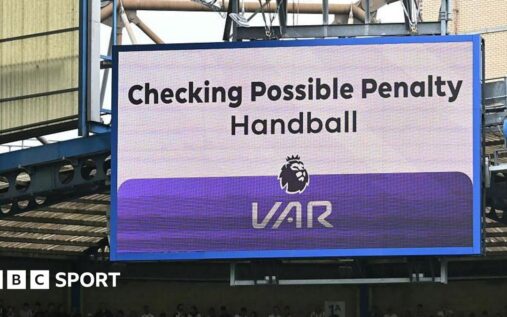 A referee reviewing a pitchside VAR monitor during a Premier League match, reflecting fan frustration with the technology.